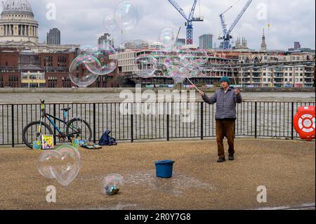 LONDON - April 21, 2023: Watch a street performer create magical bubbles on Southbank, set against London's iconic skyline with St Paul's Cathedral in Stock Photo