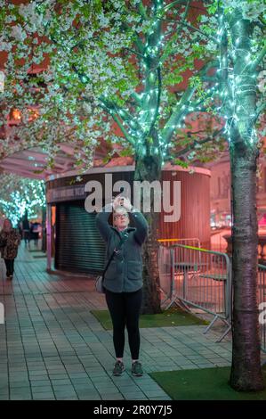 LONDON - April 21, 2023: Experience the mesmerizing blend of nature and urban architecture with illuminated trees at night next to the London Eye. Stock Photo