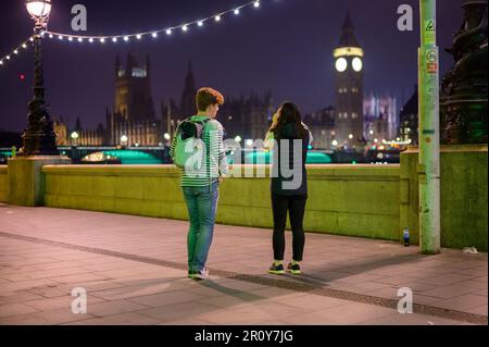 LONDON - April 21, 2023: The Southbank illuminates as tourists pause to snap photos of the iconic Houses of Parliament. Stock Photo
