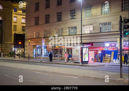 LONDON - April 21, 2023: Nighttime view of people waiting at the bus stop outside County Hall on Southbank, London at the end of Westminster Bridge. Stock Photo