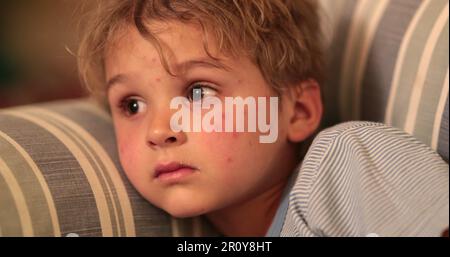 Baby toddler face watching TV screen at night on sofa at ngiht before bedtime Stock Photo