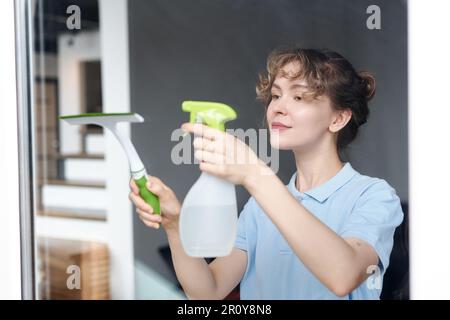 Young professional cleaner using detergent to scrubbing window in apartment Stock Photo
