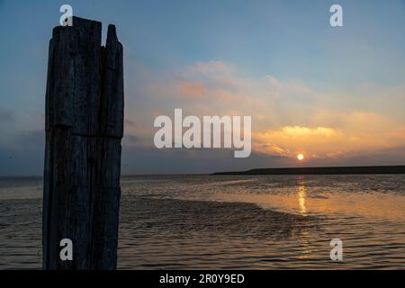 View of sun rising over dyke and mudflats during high tide on island of Texel in the Netherlands with orange coloring sky, reflection in water Stock Photo