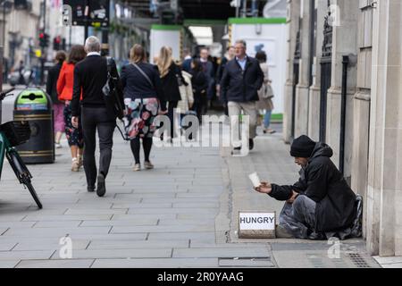 Homeless man, sat along Piccadilly with a sign stating he is hungry, holding a cup for money, Central London, England, UK Stock Photo