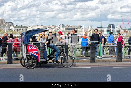 A London Rickshaw or Pedicab operating on Westminster Bridge crowded with tourists on a sunny spring day Central London England Great Britain UK Stock Photo