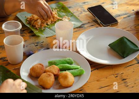 Malaysian staple breakfast on the table. Nasi lemak with Sweet desserts with coconut known as kuih ketayap and burger mini. Stock Photo