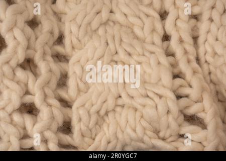 A fragment of beige knitted fabric, knitted from white sheep wool. Knitted background. Stock Photo