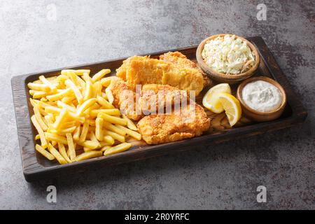 Milwaukee fish fry served with french fries, coleslaw,  tartar sauce and lemon on the wooden board on the table. Horizontal Stock Photo