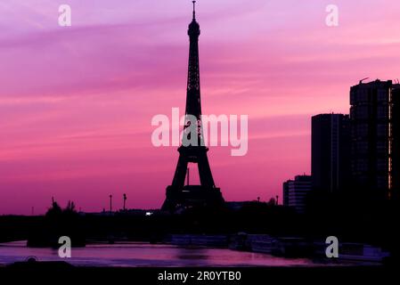 View on the Eiffel tower with group of modern buildings in front of the water of Seine river. Dramatic sky with colorful clouds. Stock Photo