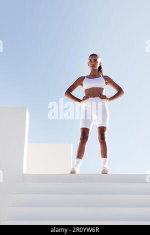 Full length of young slim sportswoman relaxing. Woman with hands on hips standing on the top of stairs. Stock Photo