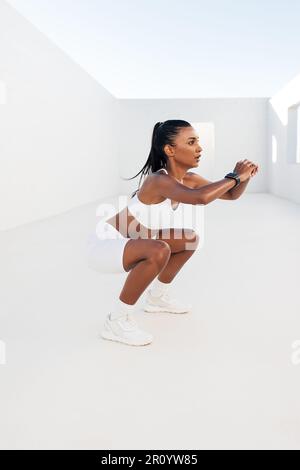 Slim woman practicing sit-ups in the white outdoor studio. Fitness female doing exercises for legs and glutes. Stock Photo