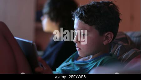 Child watching content on tablet at night. Young boy staring at tech device screen Stock Photo