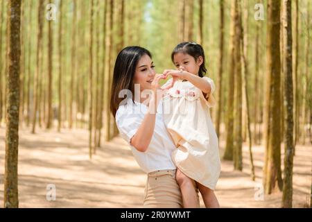 Mother holding daughter and making heart by hands together in park Stock Photo