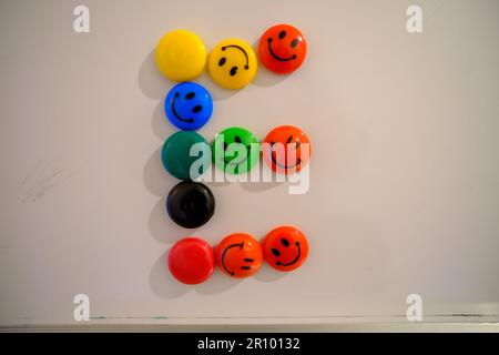 Multicolored round whiteboard magnets are placed on the blackboard in the form of the letter E Stock Photo