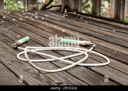 heavy fitness jump rope on a rustic, weathered wooden backyard deck in springtime scenery Stock Photo