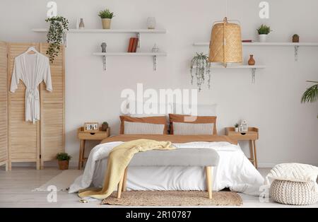 Interior of stylish bedroom with bed and houseplants on shelves Stock Photo