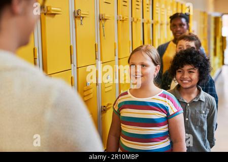 We like to do affirmations before going into class. a diverse group of children lining up outside their classroom at school to greet their teacher. Stock Photo