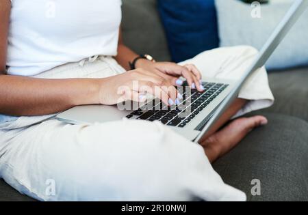 My inbox is overflowing. an unrecognizable woman sitting alone on her sofa and using her laptop to work from home. Stock Photo