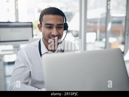 Let me sort that out for you. a handsome young businessman sitting alone in his office and wearing a headset while using his laptop. Stock Photo