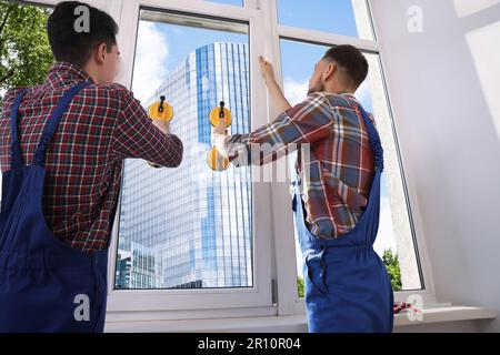 Workers using suction lifters during plastic window installation indoors Stock Photo