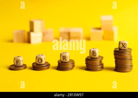 Word Forex made of wooden cubes with letters on stacked coins against yellow background Stock Photo