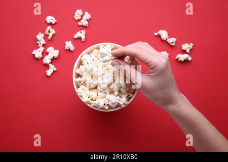 Woman taking delicious popcorn from paper bucket on red background, top view Stock Photo