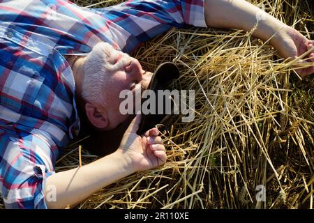 Senior old farmer in the straw hay. Senior taking a break and relaxing on a hay on an summer day. Grandfather laying on haystack in countryside Stock Photo