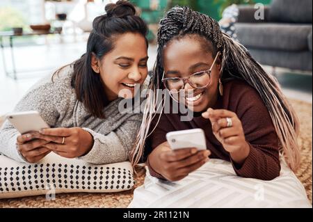 Aaaandsend. two young women using their smartphones on the floor at home. Stock Photo