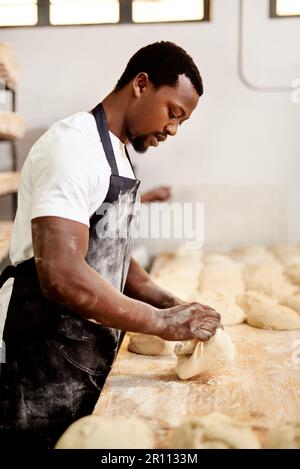 Doing it just how my grandma taught me. a male baker busy shaping dough at work. Stock Photo