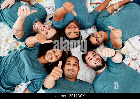 Nothing but good vibes here. Cropped portrait of a diverse group of friends lying down and showing a thumbs up after an art class. Stock Photo