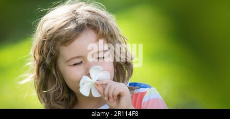 Close up face of cute child outdoors. Spring banner for website header. Funny child smelling plumeria flower, face close up. Kids in summer nature Stock Photo