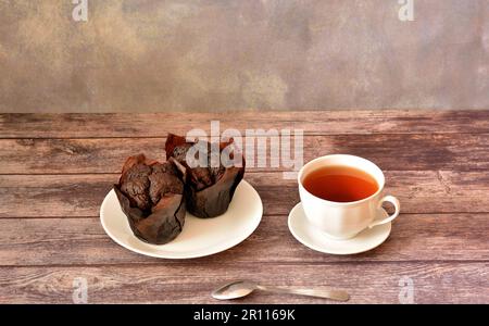 A plate with two fresh chocolate muffins and a cup of hot tea on a wooden table. Close-up. Stock Photo