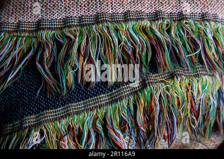close up of tassels or fringe on a blanket containing blue, black, red, yellow, green and white Stock Photo