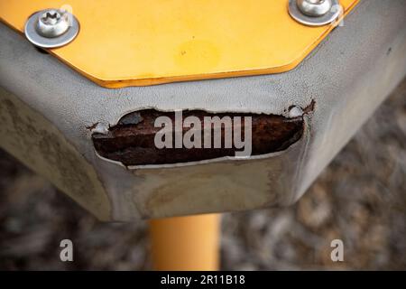 close up of worn, weathered, yellow playground equipment with a tear in the coating over the metal Stock Photo