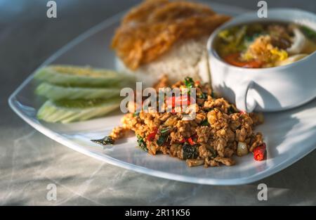 Thai spicy meal, Moo Pad Kaprow, or stir-fried ground pork with basil with white rice. Pork basil on a white plate with a Thai omelet over jasmine ric Stock Photo