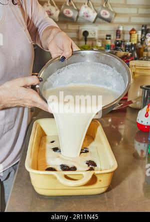Chef puts the dough into ceramic mold with plums to make plum cake. Stock Photo