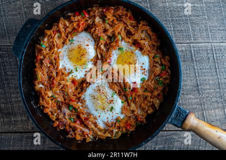 Stewed cabbage with vegetables and fried eggs in a frying pan on a wooden background, close up, top view. Food background. Healthy food Stock Photo