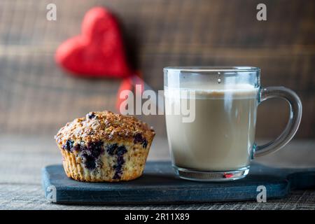 Delicious muffin with blueberries and cappuccino glass cup on a wooden table, close up. Fresh cupcake and coffee for breakfast Stock Photo