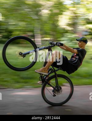 A young man in casual clothing, riding a bicycle, performing a stunt of mid-air flip Stock Photo