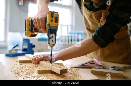 Carpenter working with drill leaning over table at carpentry workshop Stock Photo