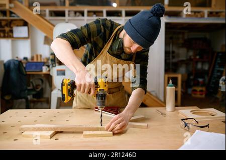 Young man jointer working with drill leaning over table at carpentry workshop Stock Photo