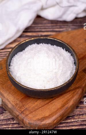 Coconut powder. Grounded coconut flakes on wood floor. Dark bowl of dessicated coconut. Close up Stock Photo