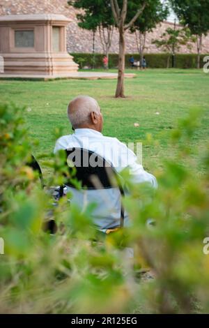 old man isolated sitting alone at iron chair at park from back at evening Stock Photo