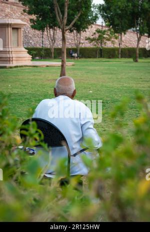 old man isolated sitting alone at iron chair at park from back at evening Stock Photo