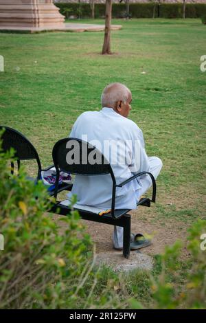 old man isolated sitting alone at iron chair at park from back at evening Stock Photo