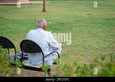 old man isolated sitting alone at iron chair at park from back at evening Stock Photo