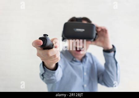 Young man trying virtual reality at home, using headset VR glasses and holding joystick, playing video games. Modern technologies and domestic enterta Stock Photo
