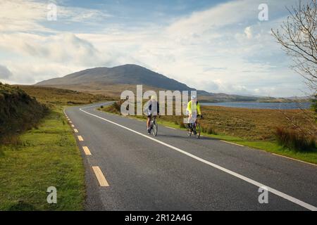 Group of people cycling trough scenic nature by the lough inagh with mountains in the background at Connemara National park in county Galway, Ireland Stock Photo