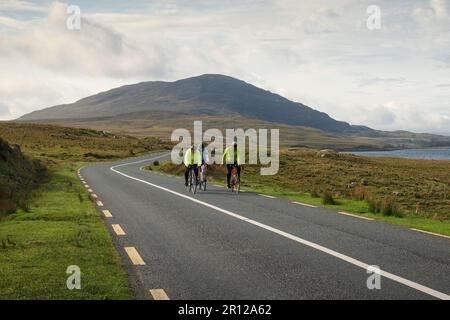 Group of people cycling trough scenic nature by the lough inagh with mountains in the background at Connemara National park in county Galway, Ireland Stock Photo