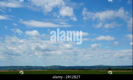 Countryside landscape wallpaper with serene blue sky with fluffy white clouds above crops field and hills on beautiful summer day Stock Photo